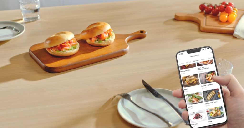 person holding phone filled with recipes in front of sandwiches on a cutting board