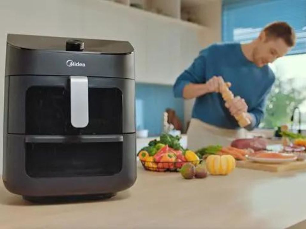 A Midea air fryer with a man prepping food in the background.