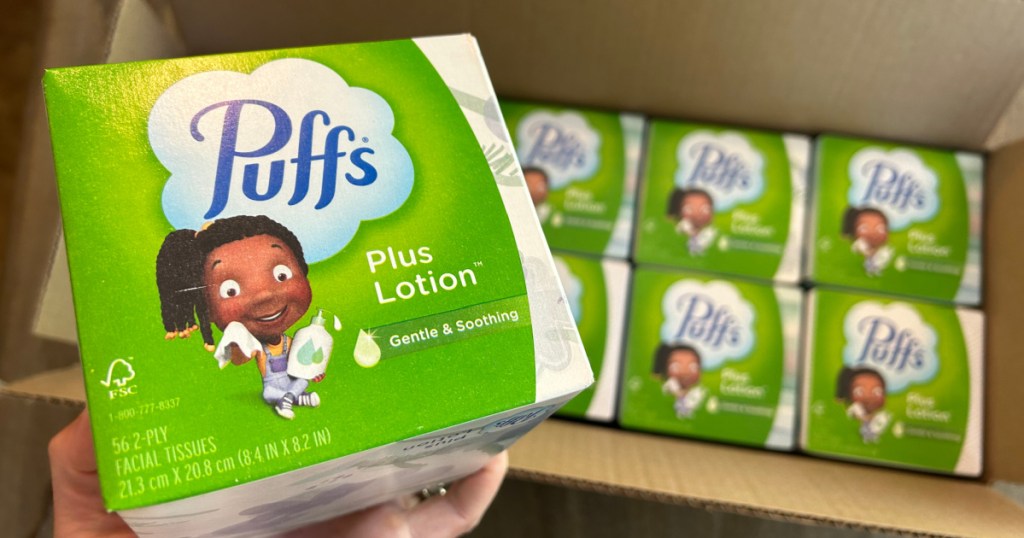 person holding green colored box of Puffs Plus Lotion with more boxes displayed