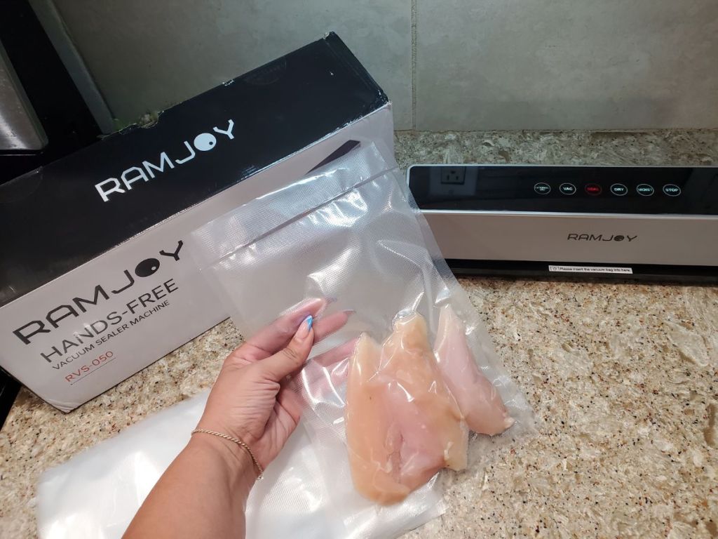 Woman's hand holding a seal back of chicken after using the RAMJOY Hands Free Vacuum Food Sealer