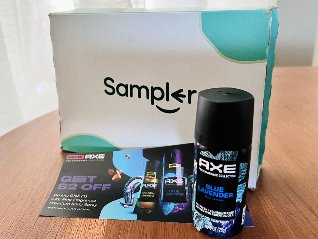 A bottle of Axe body spray and coupons in front of a Sampler box on a table 