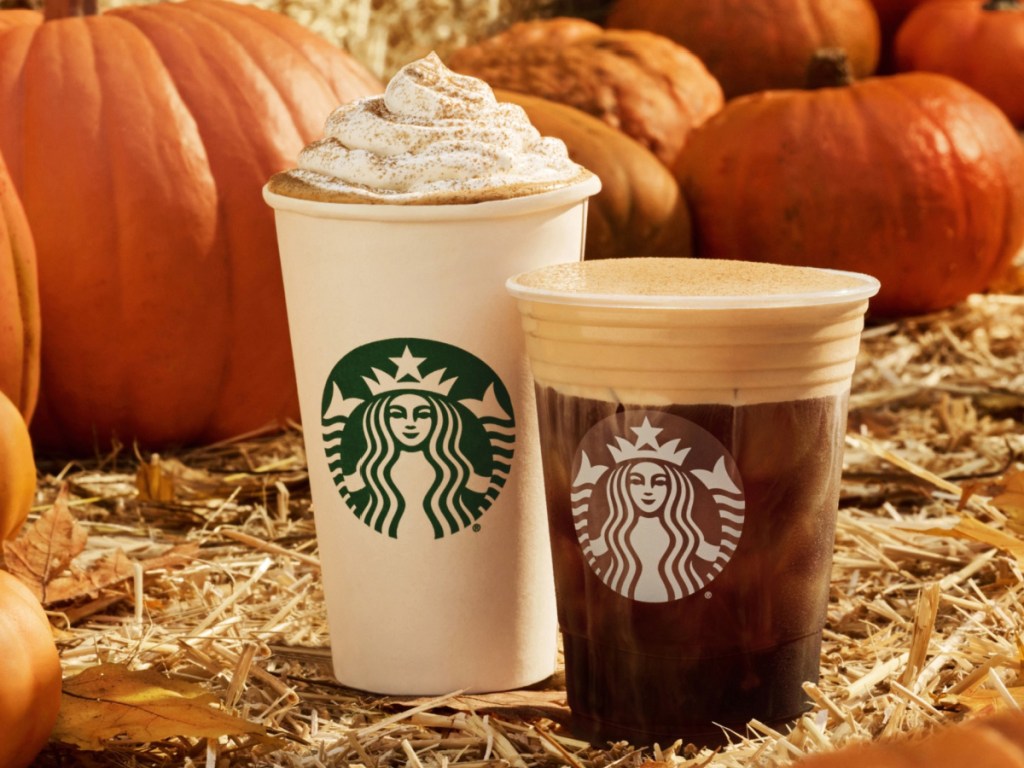 Starbucks hot and cold drinks on barrel of hay surrounded by pumpkins