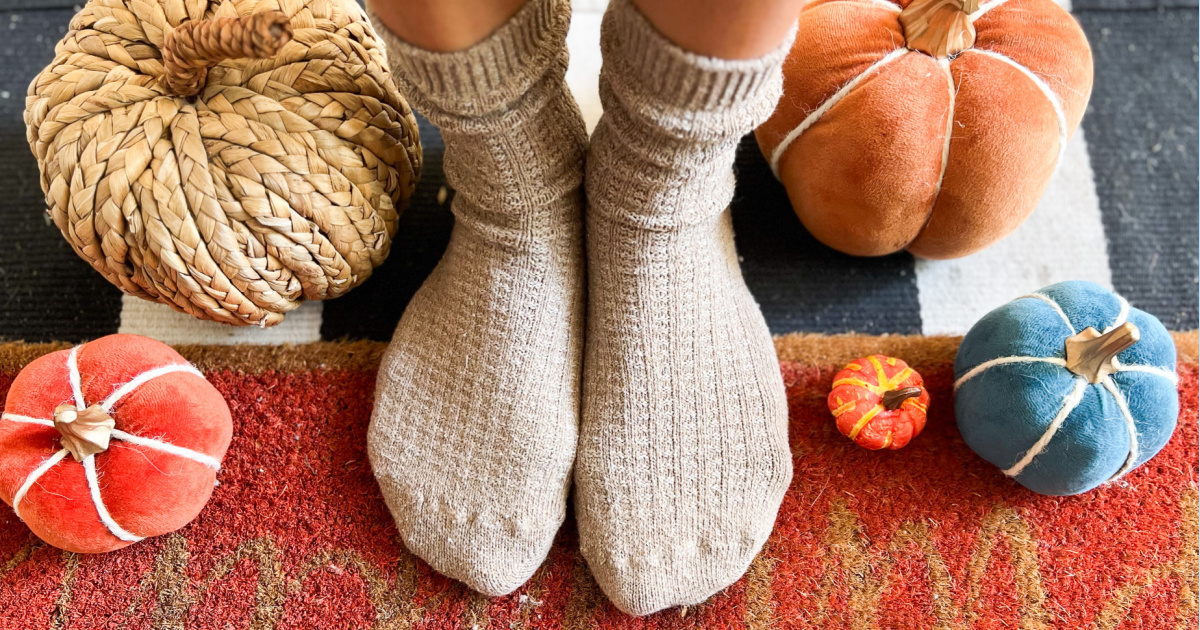 women's feet wearing waffle style socks standing on fall doormat near pumpkin decorations