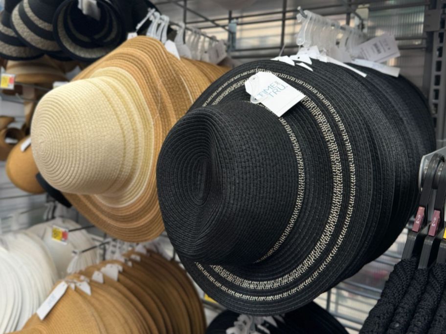 a natural colored and black straw panama hats hanging on pegs on a store aisle