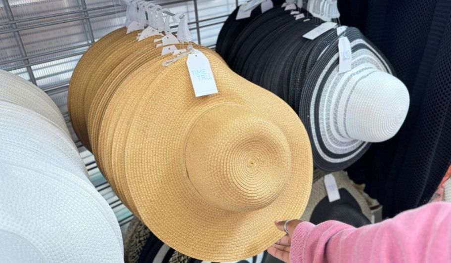 a womans hand hold the brim of a natural colored floppy straw hat