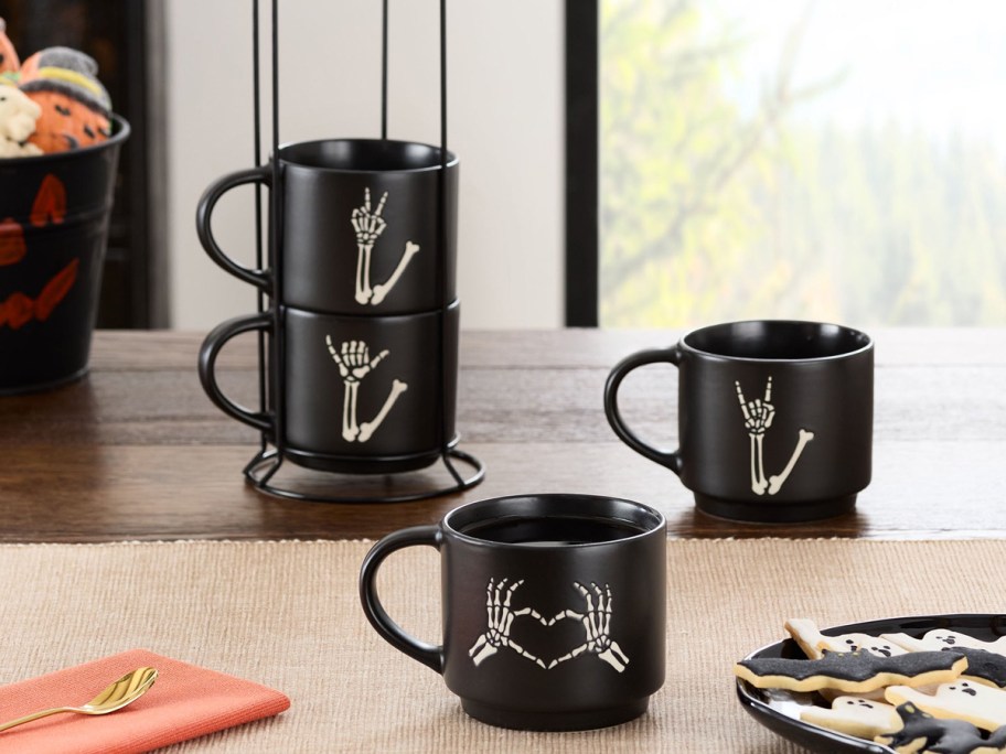 set of 4 black skeleton hand mugs on table