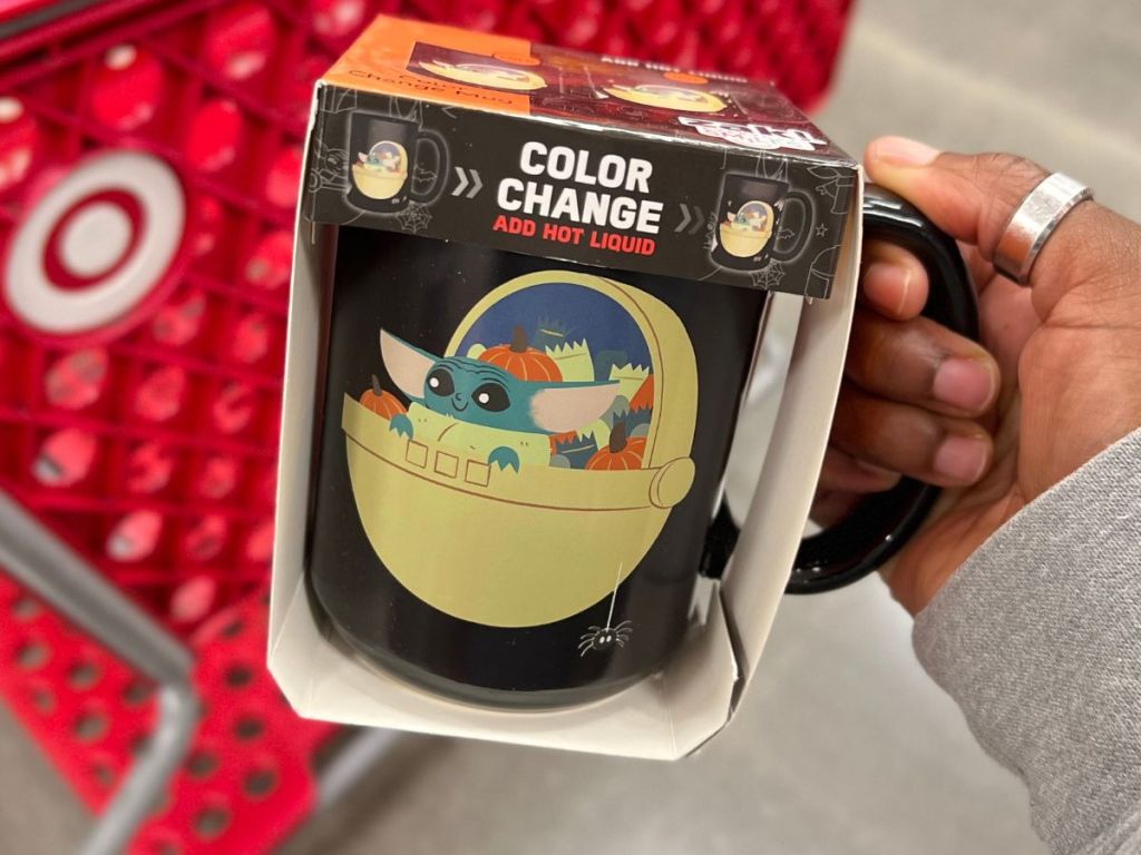 A hand holding a Zak Grogu Color Changing Mug in front of a Target cart