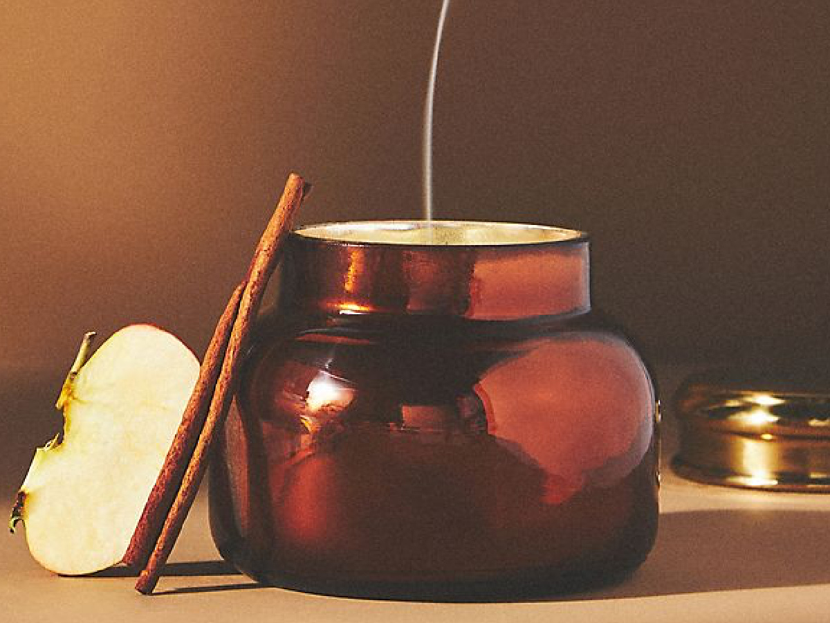 anthropologie capri blue spiced cider candle displayed with a cinnamon stick and an apple-2
