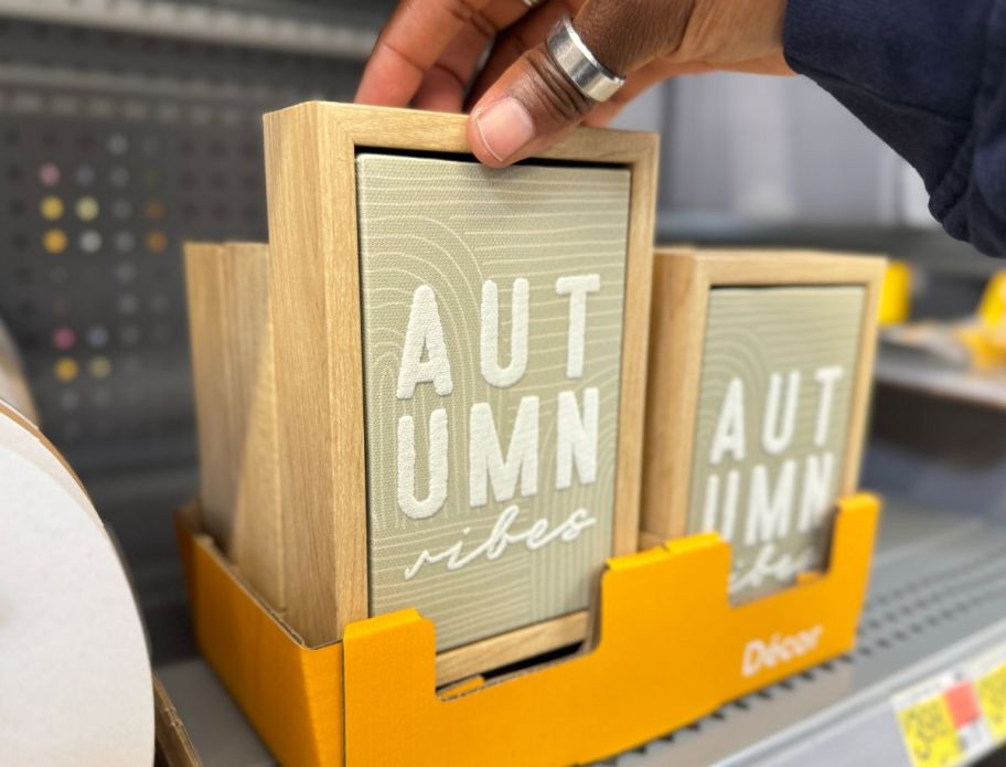 a woman's hand holding a wooden fall wall decor