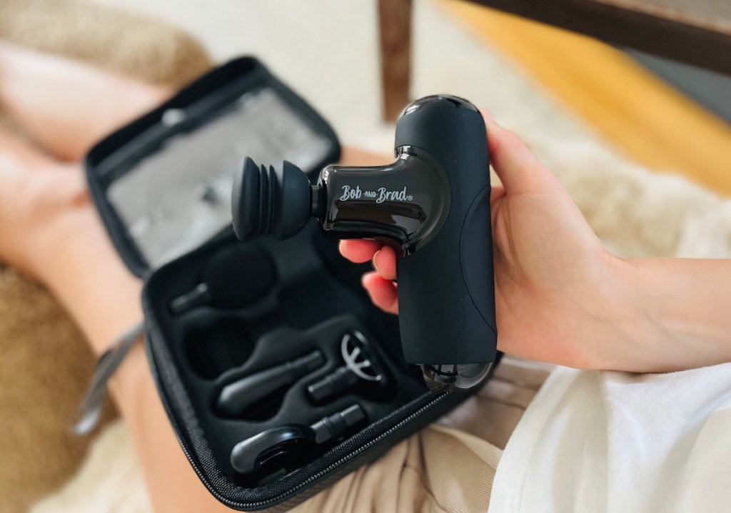 hand holding black mini massage gun with travel case sitting on lap