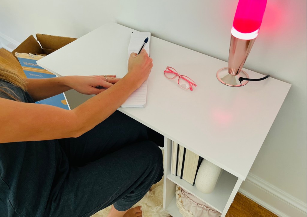 person sitting at small writing desk next to lava lamp