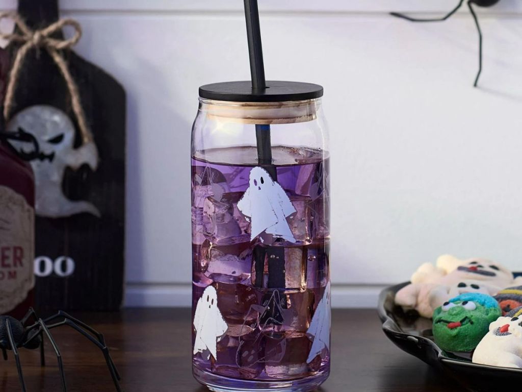 ghost cup with lid and straw with purple liquid in it on table next Halloween cookies
