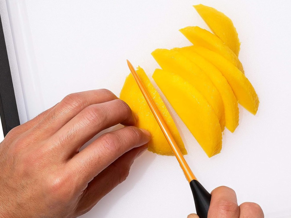 hand using mango slicer to cut mango on a. cutting board