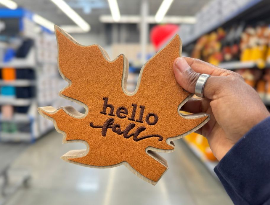 a woman's hand holding a leaf-shaped wooden fall wall decor