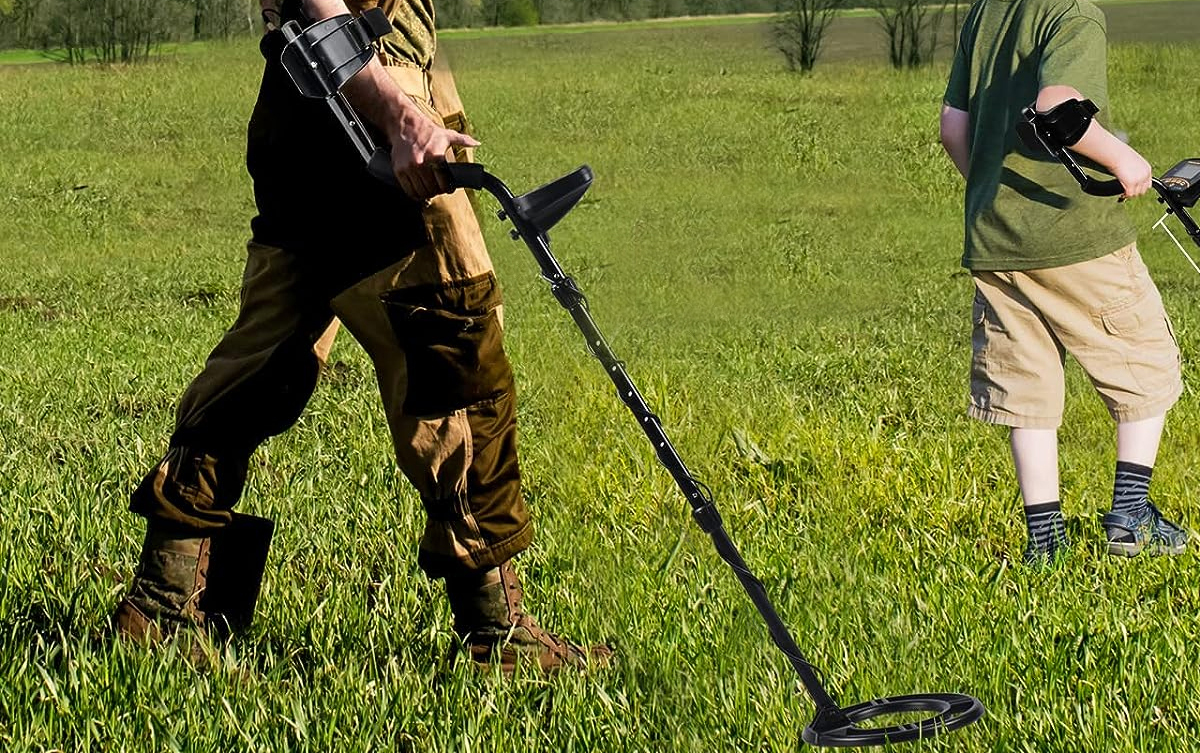 man using metal detector in grass