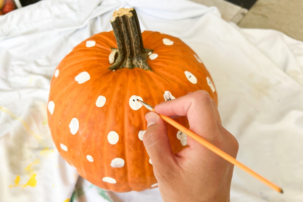 hand painting black eyes on ghosts on pumpkin