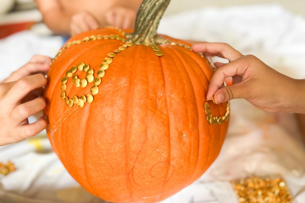 multiple hands pressing tacks into pumpkin