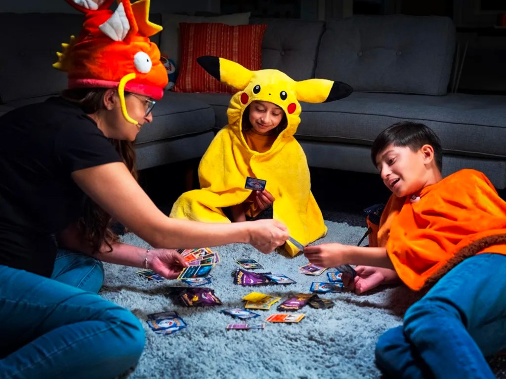 two kids and mom wearing pokemon costumes playing with cards