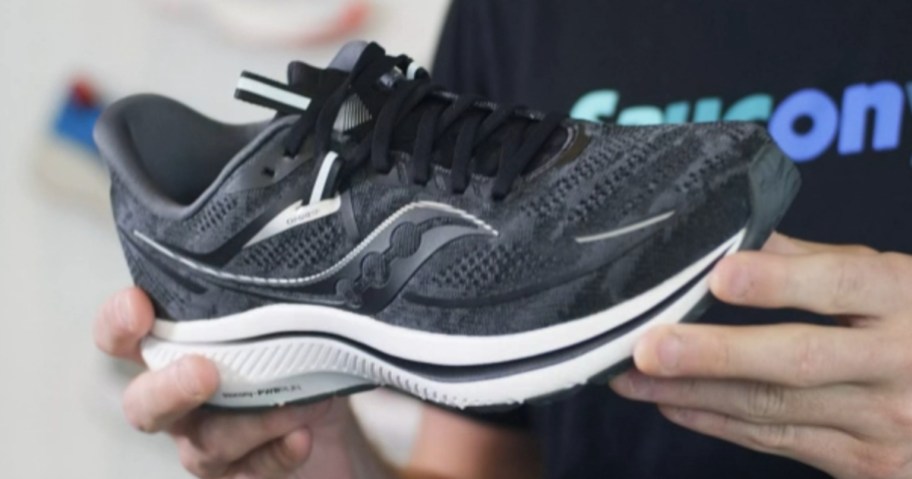 hands holding a single black and white Saucony running shoe