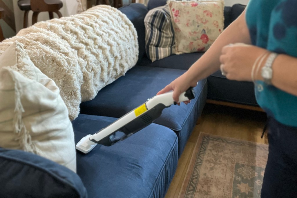 woman using stick vac on blue couch