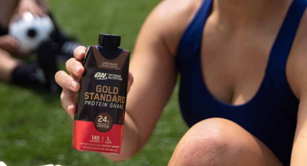 soccer player holding premium protein in chocolate in her hands as she sits on grass