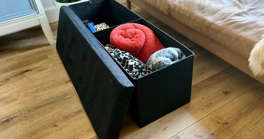 black storage ottoman with blankets and pillows inside