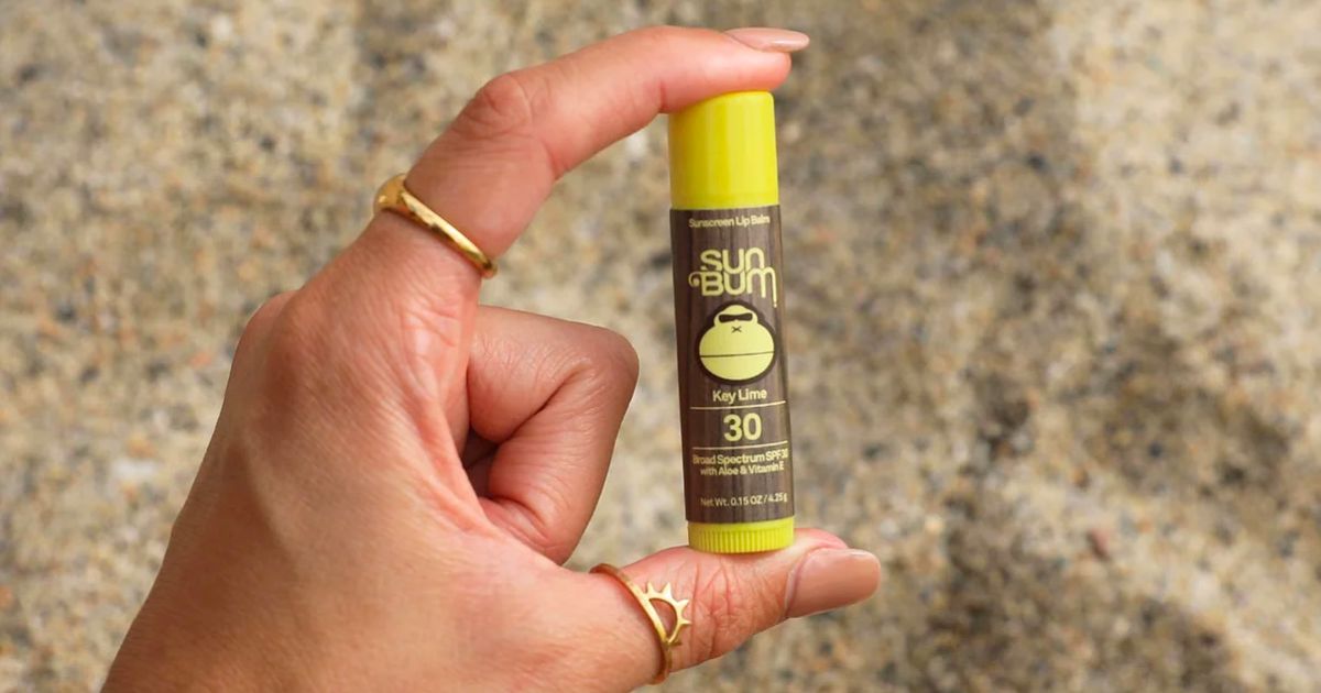 a woman's hand holding a tube of spf 30 key lime lip balm