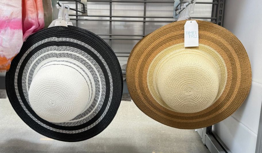2 striped brim straw hats hanging on pegs on a store aisle