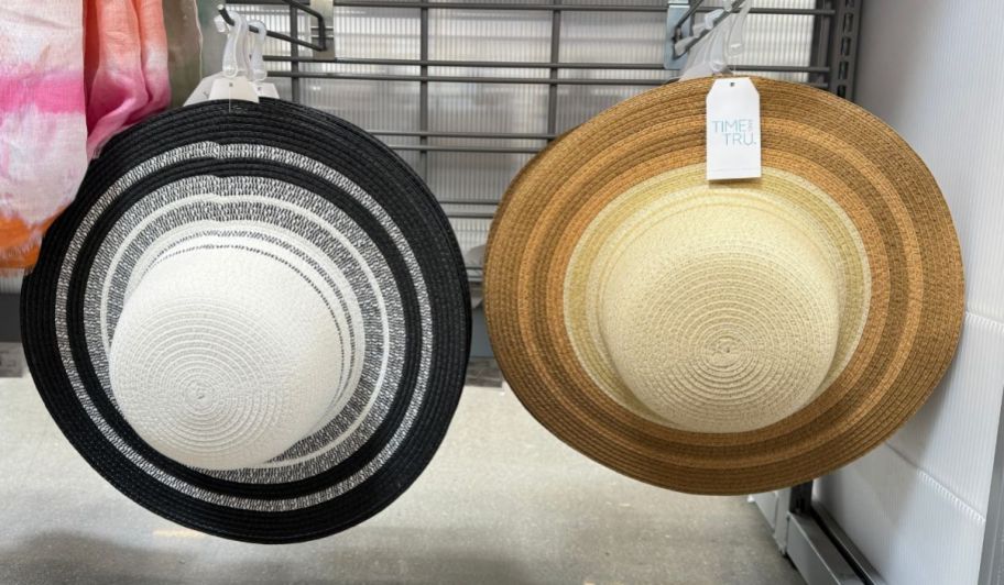 2 striped brim straw hats hanging on pegs on a store aisle