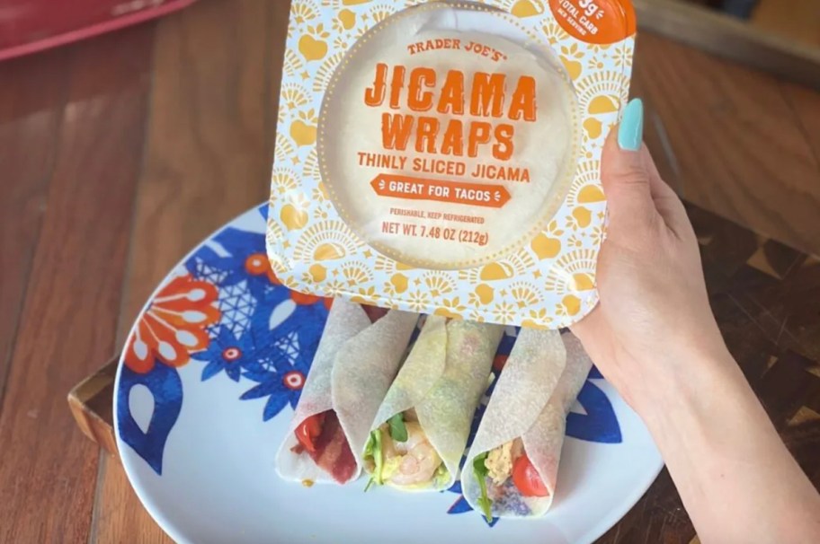hand holding a pack of trader joes jicama wraps over plate of tacos