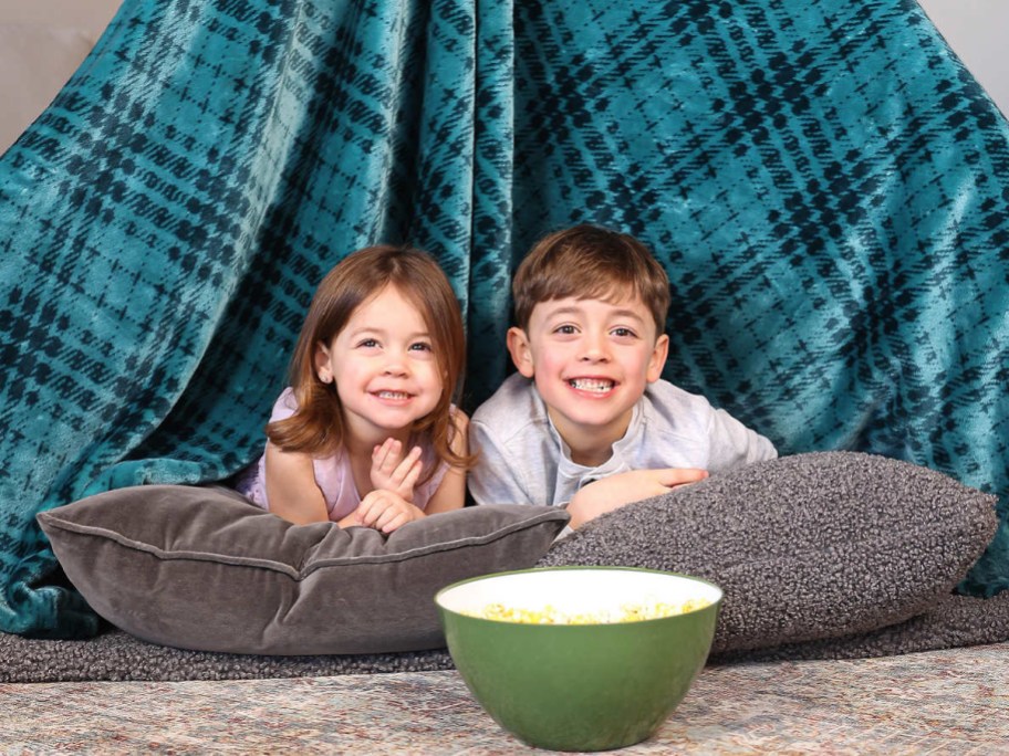 two kids playing on the floor with huge blanket as a fort