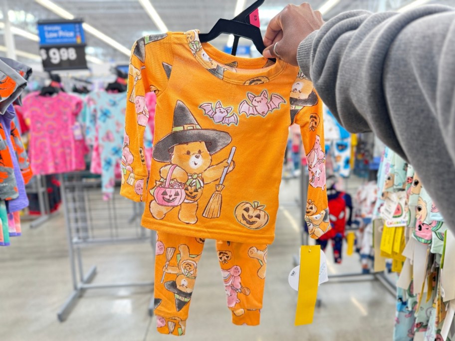 hand holding a set of orange toddler Halloween pajamas with Care Bears on them