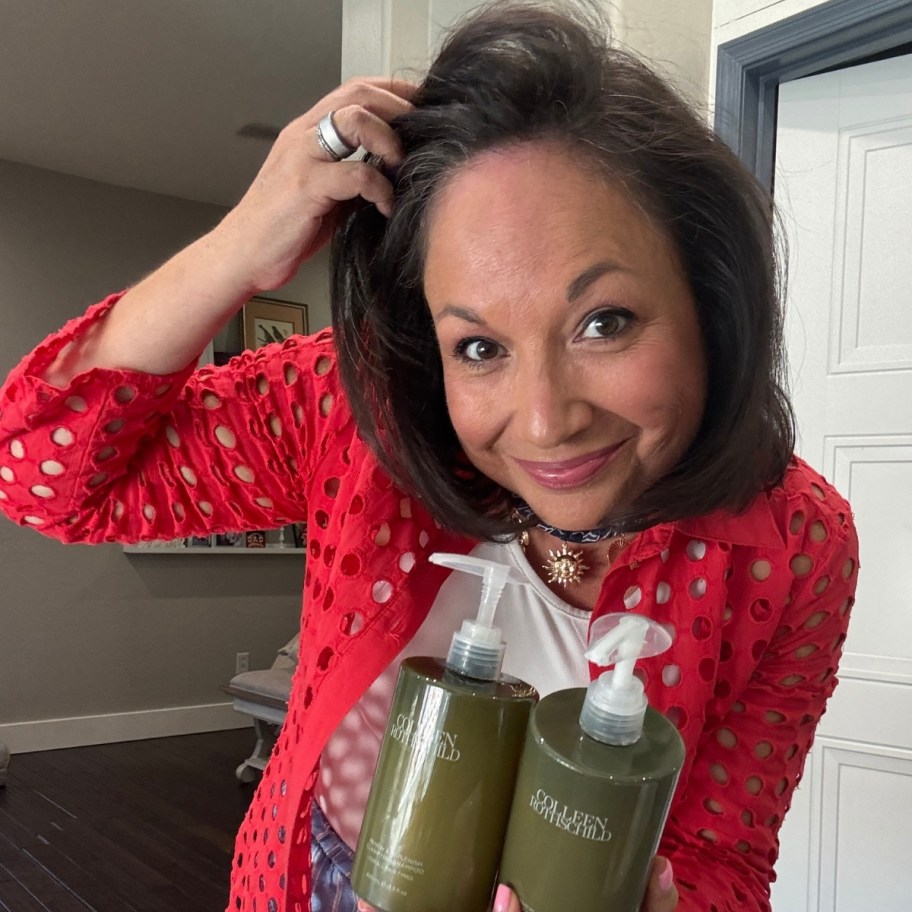 a woman holding bottles of shampoo and conditioner in one hand with her other hand in her hair