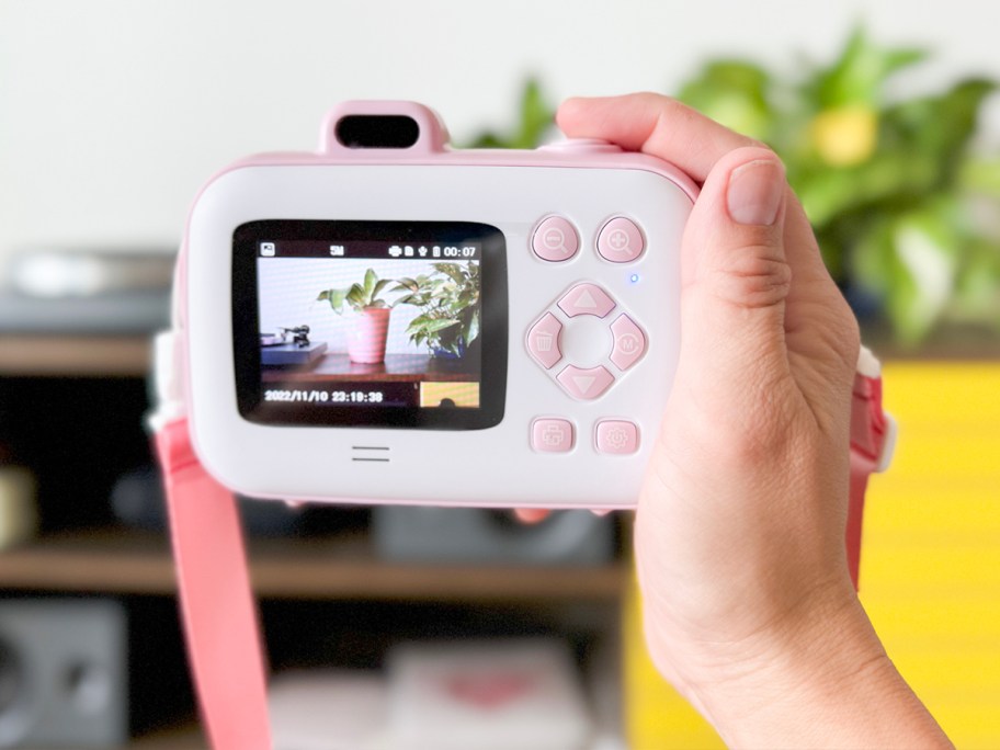 hand holding pink and white camera with back showing 
