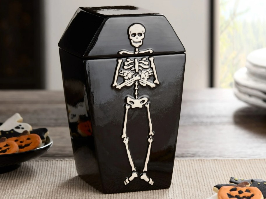 black coffin shaped cookie jar with a skeleton on it on a kitchen counter