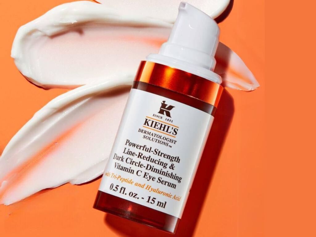 bottle of Kiehl's Powerful-Strength Dark Circle Reducing Vitamin C Eye Serum on orange background with cream behind it