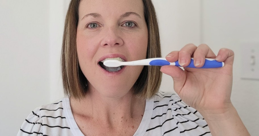 woman brushing her teeth with a white and blue flossing toothbrush