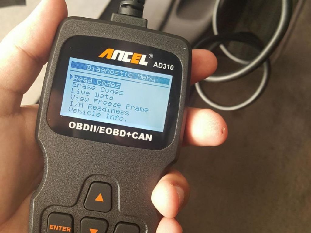 ANCEL AD310 Classic Enhanced Universal OBD II Scanner Car Engine Fault Code Reader in person's hand sitting in a car showing the menu in person's hand