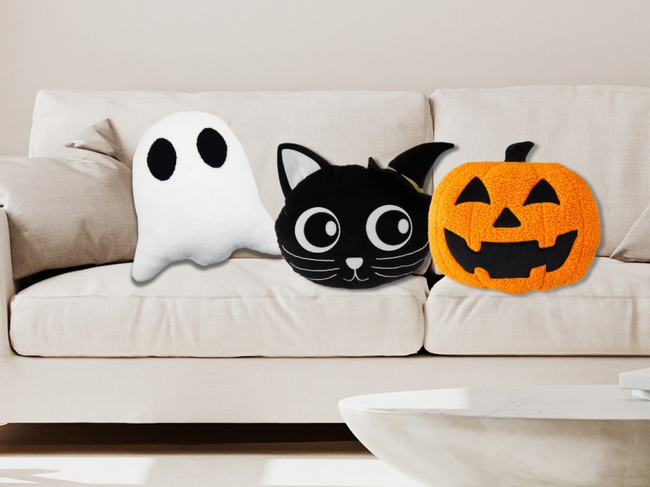 cream color sofa with a white ghost pillow, black cat pillow, and orange jack-o-lantern pillow