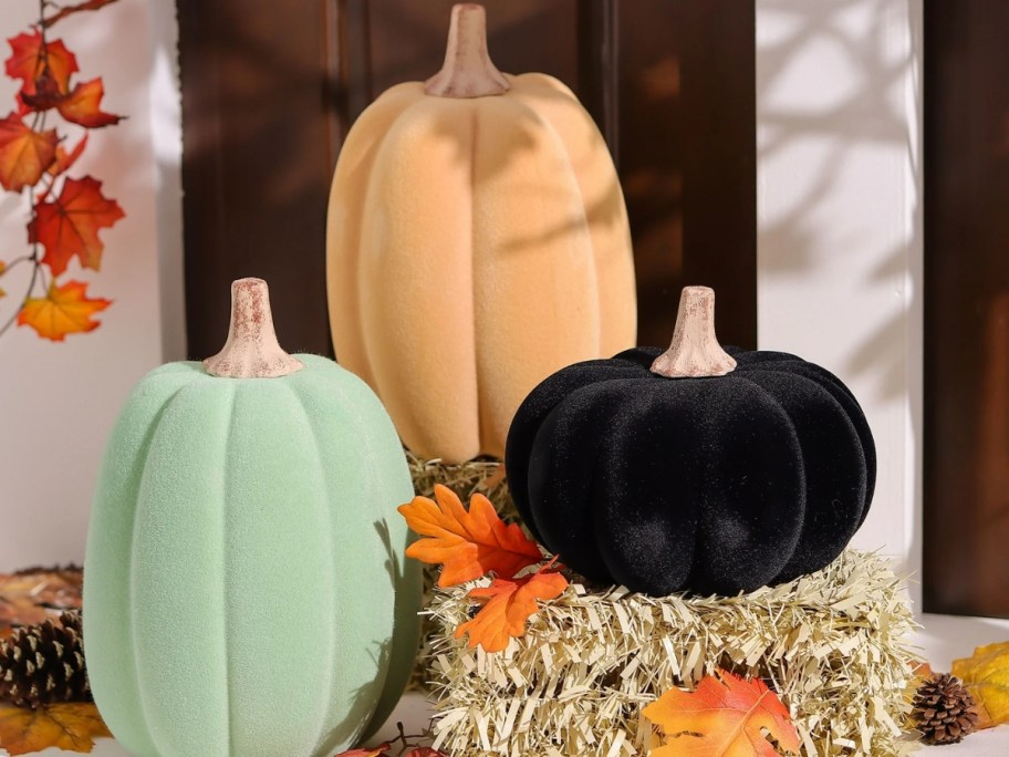 green, orange, and black flocked pumpkins around fall decor on a porch