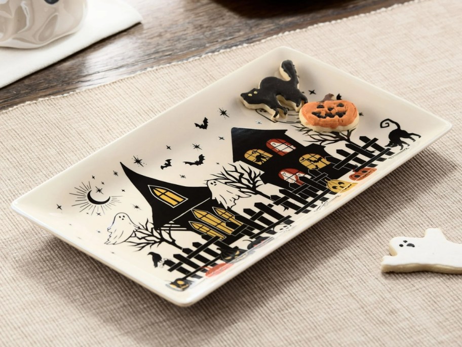 cream serving tray with haunted houses and ghosts with cookies on it on a counter