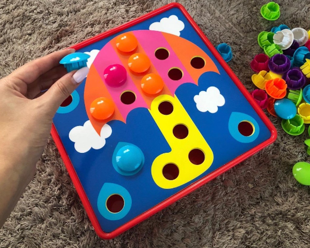 fingers holding blue peg piece over pegboard art best toys for 2 year olds