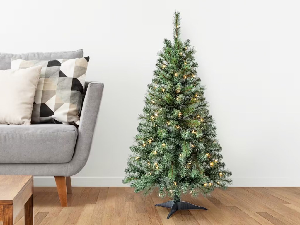 small artificial christmas tree with white lights next to grey couch