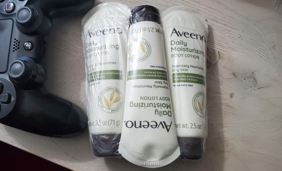 3 travel size tubes of aveeno daily lotion in shrink wrap next to a video game controller