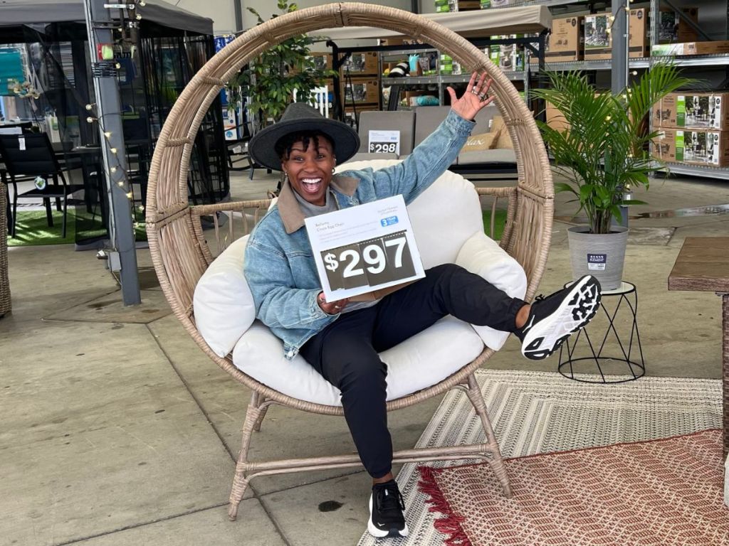 woman smiling and holding price sign while sitting in a large round wicker egg chair garden center at Walmart