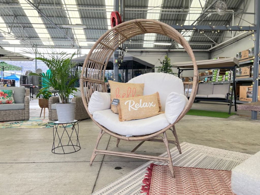 large round wicker egg chair with cushions and decorative pillows in lawn and garden center at Walmart