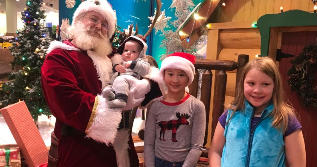 Santa holding a baby while standing next to 2 kids