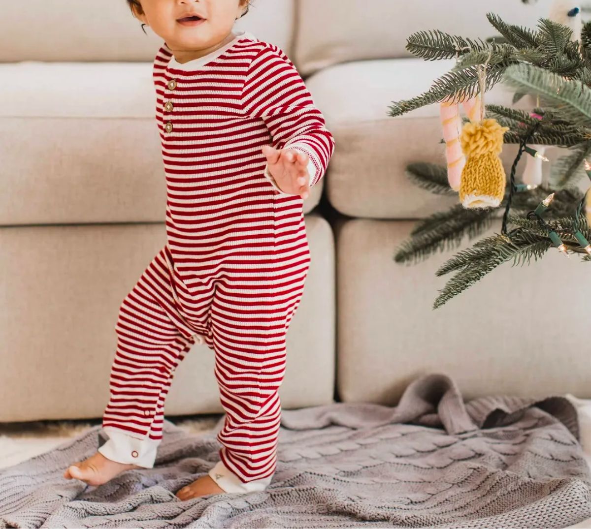 a baby taking a step next to a christmas tree wearing a burts bees baby Classic Stripe Thermal Jumpsuit 