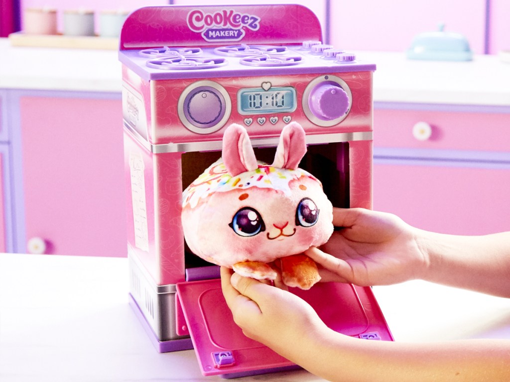 child taking a plush toy out of a pink Cookeez Makery Oven