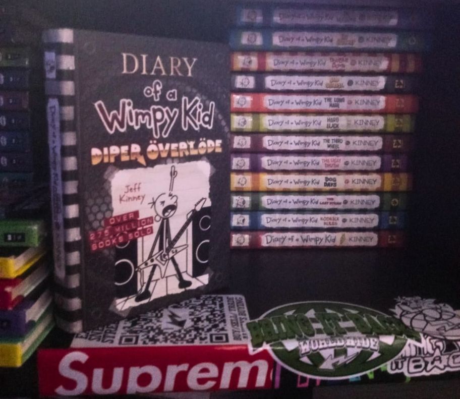 diary of a wimpy kid diper overlode book pictured next to a stack of the other books in the series